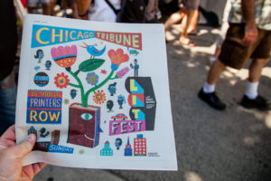 A hand holds a newspaper. Its cover showcases the Printers Row Lit Festival.