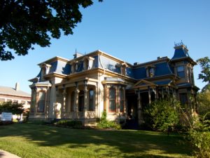 Lush greenery surrounds a lavishly built historic victorian house.